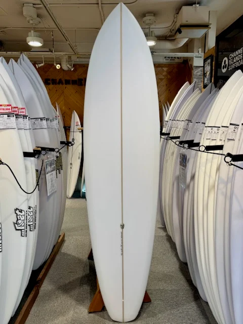 IMG_1863-1 - SHOP NEWS | ムラサキスポーツオンラインストア 通販 White surfboard displayed upright on a stand in a surf shop, with rows of other boards on either side.