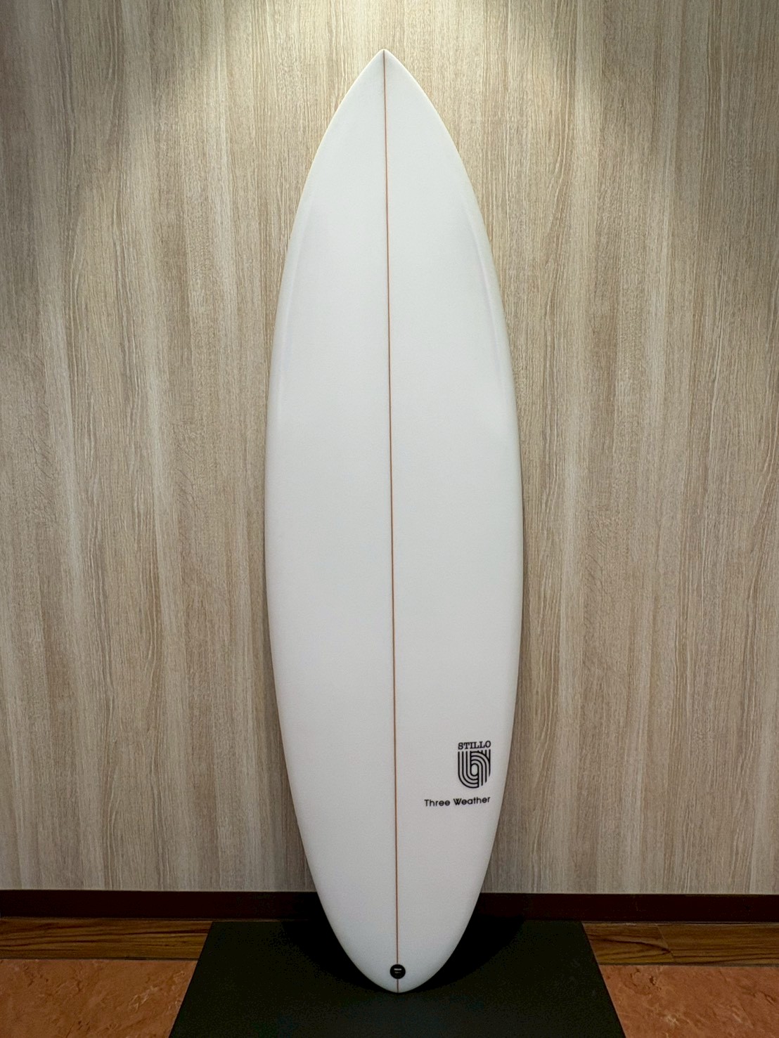 LINE_ALBUM_2026 TW_260422_10 - SHOP NEWS | ムラサキスポーツオンラインストア 通販 White surfboard with a thin red stringer standing upright against a wood-paneled wall on a black mat.