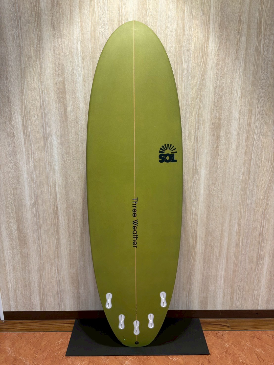 LINE_ALBUM_2026 TW_260422_2 - SHOP NEWS | ムラサキスポーツオンラインストア 通販 Olive-green surfboard standing upright against a wall, with a vertical stringer and six white fin boxes at the base, SOL logo on the right.