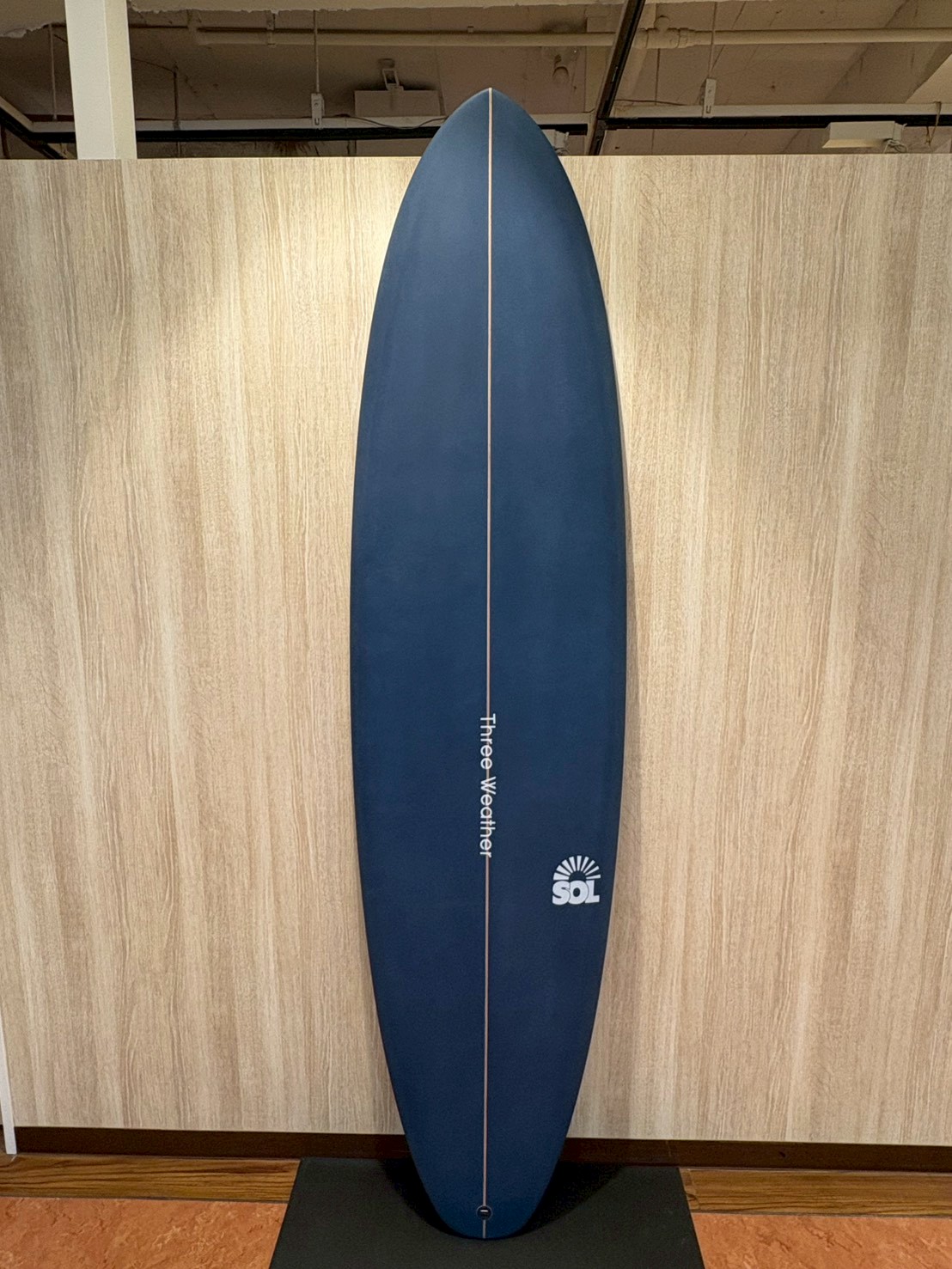 LINE_ALBUM_2026 TW_260422_3 - SHOP NEWS | ムラサキスポーツオンラインストア 通販 Blue surfboard on a display stand in a showroom, with a white center seam and an SOL logo near the bottom.