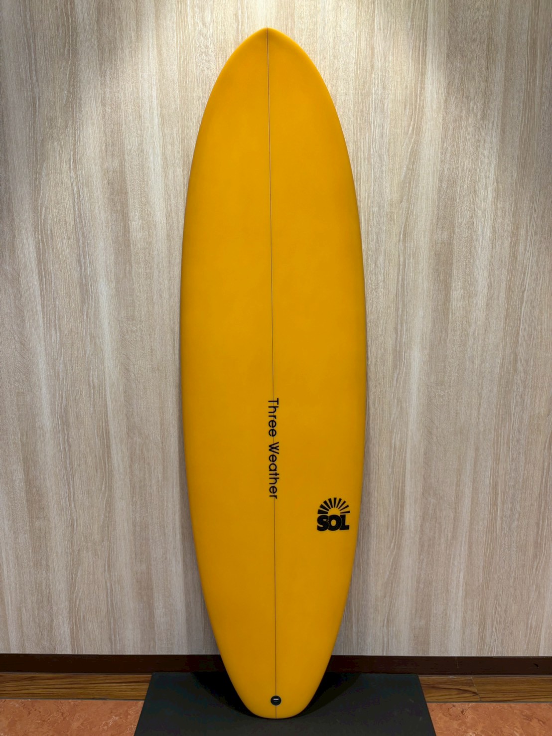 LINE_ALBUM_2026 TW_260422_5 - SHOP NEWS | ムラサキスポーツオンラインストア 通販 Yellow surfboard standing upright against a light wood wall, with 'Three Weather' branding along the center and a SOL logo near the bottom.