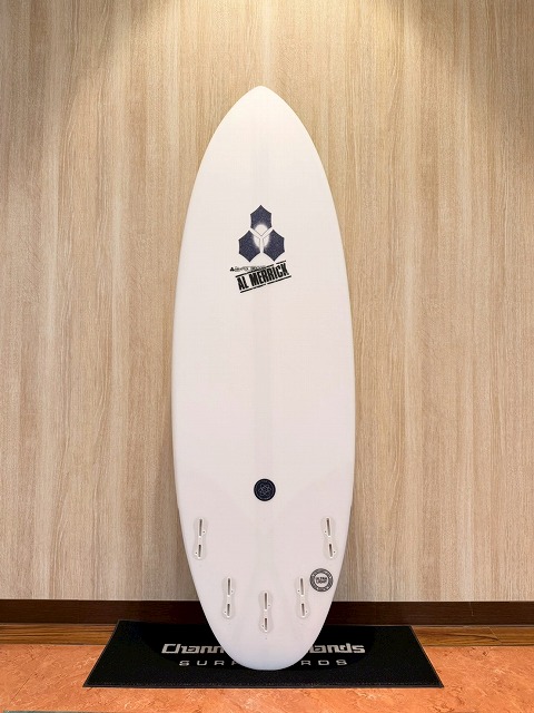 s-LINE_ALBUM_2026 CI_260522_2 - SHOP NEWS | ムラサキスポーツオンラインストア 通販 White surfboard standing upright against a light wood wall, logo near the top, four fin boxes along the bottom footer, placed on a black mat.
