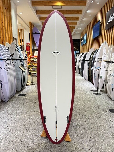 a-IMG_2673 - SHOP NEWS | ムラサキスポーツオンラインストア 通販 White surfboard with maroon rails displayed upright in a surf shop showroom.