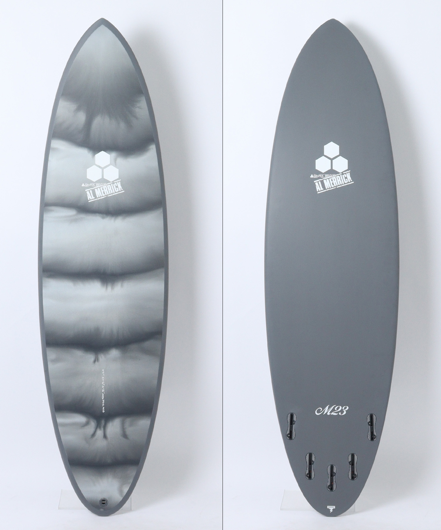 Two views of a snowboard: left shows a glossy metallic top with cloud-like patterns and a hex logo, right shows a solid gray bottom with a hex logo and 'M23' near the tail.