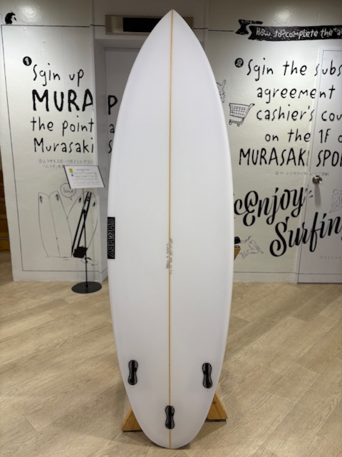 IMG_7104 - SHOP NEWS | ムラサキスポーツオンラインストア 通販 White surfboard with a thin yellow stringer, mounted upright on a wooden display stand in a gallery, with wall texts in the background.