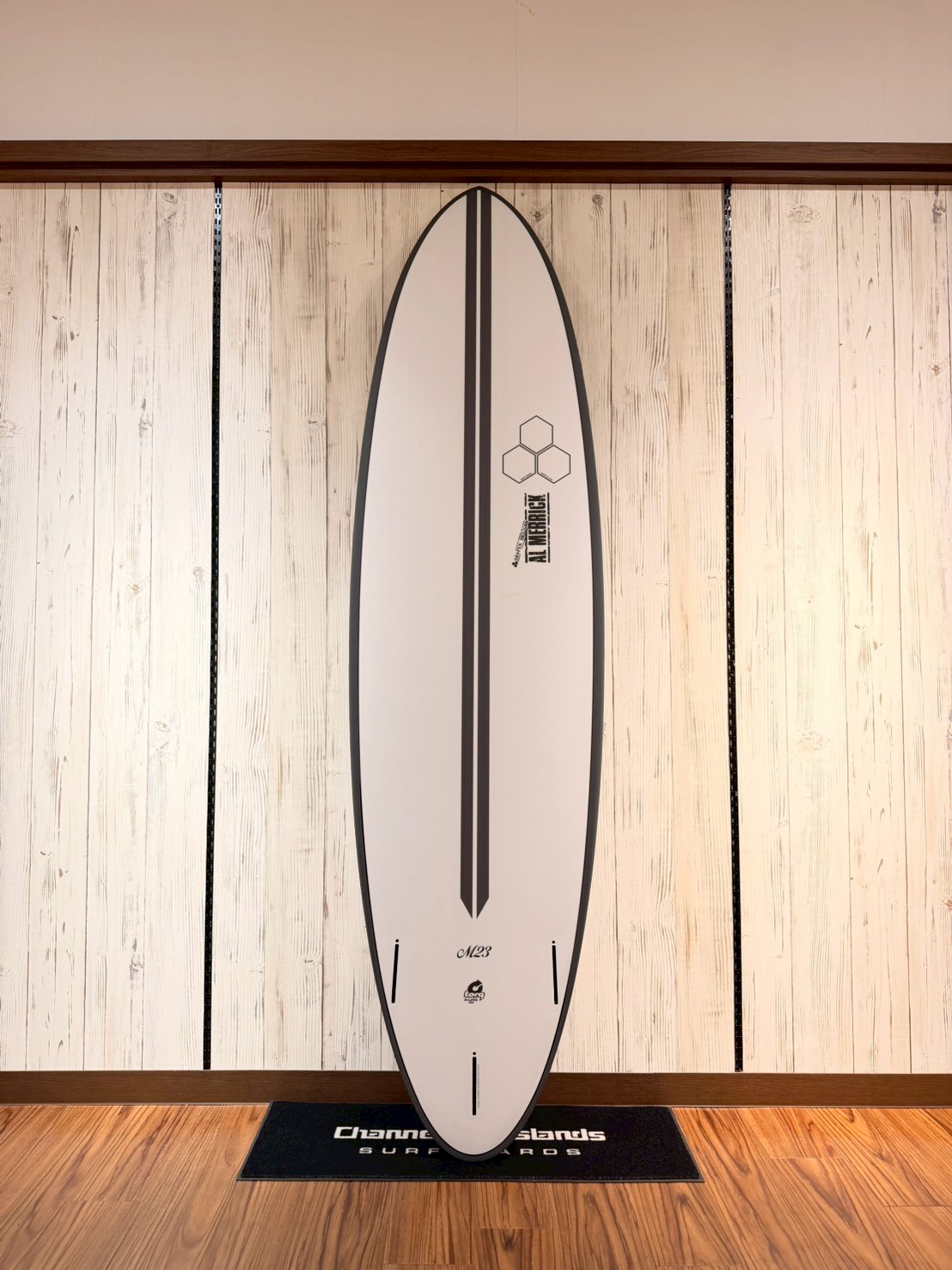 LINE_ALBUM_2026 トルク_260426_10 - SHOP NEWS | ムラサキスポーツオンラインストア 通販 White surfboard with a black central stripe, mounted vertically on a white wood-paneled wall.