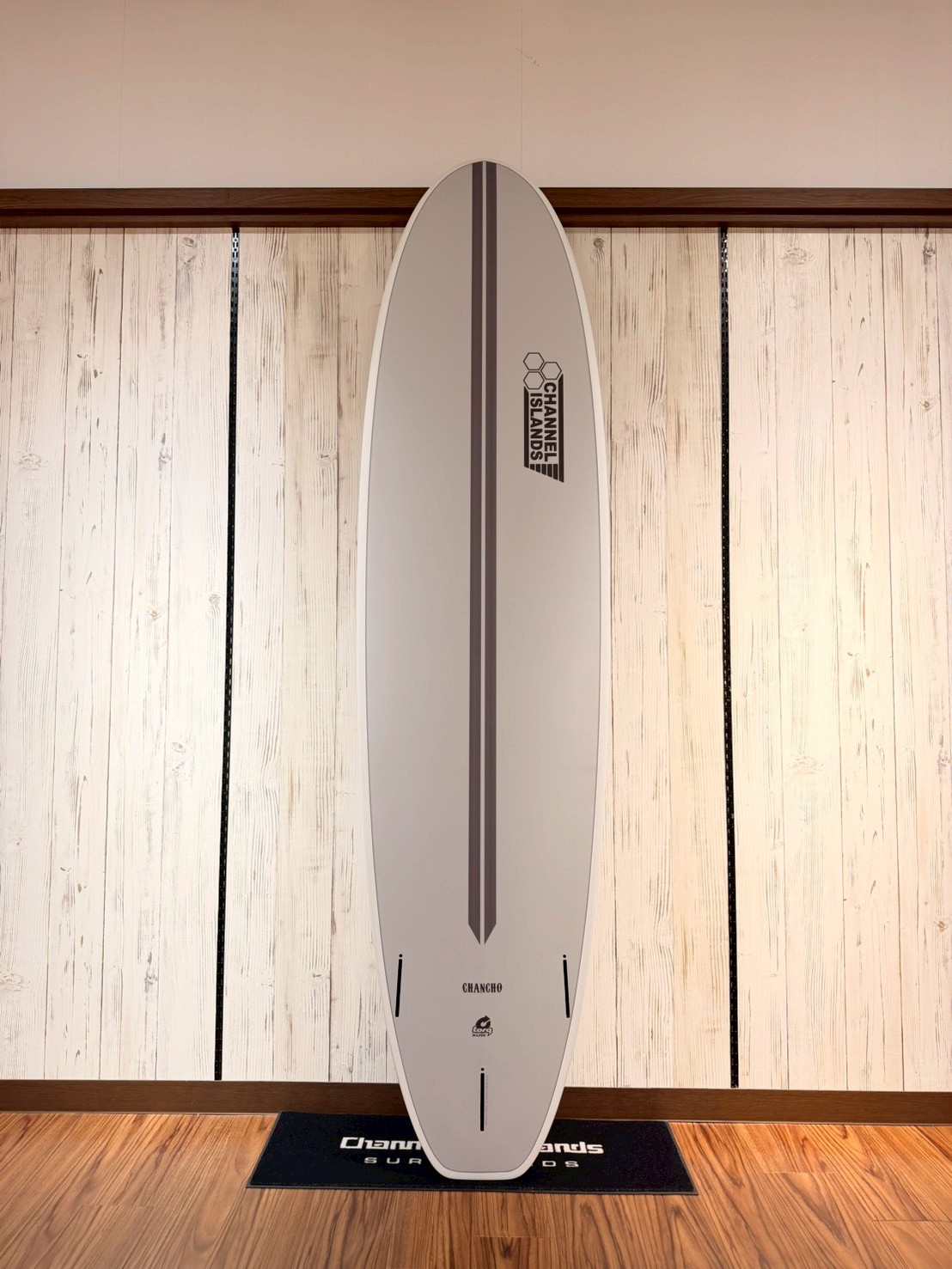 LINE_ALBUM_2026 トルク_260426_8 - SHOP NEWS | ムラサキスポーツオンラインストア 通販 White surfboard standing upright indoors on a display mat, with a vertical dark stripe and Channel Islands logo near the top.