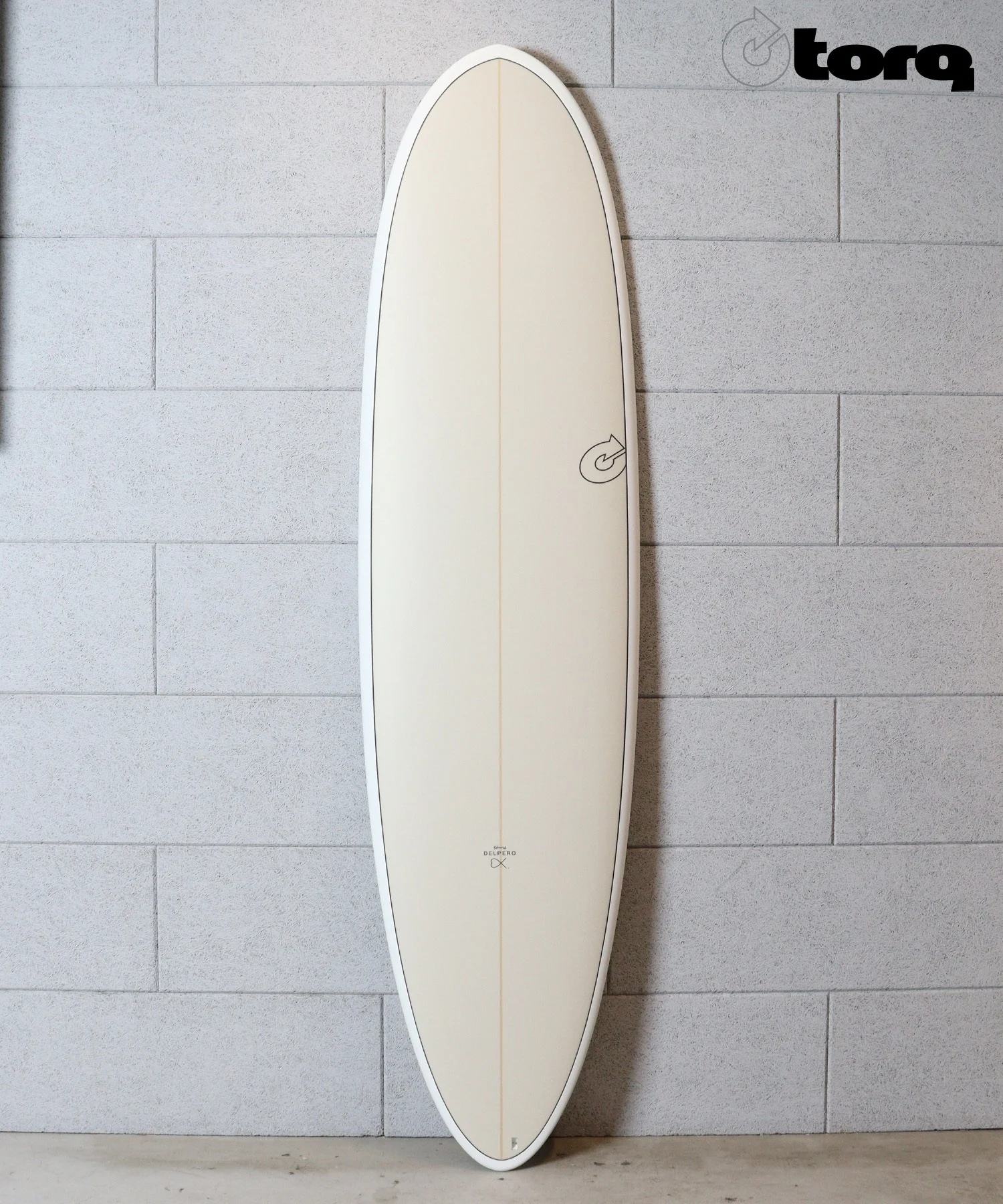 image - SHOP NEWS | ムラサキスポーツオンラインストア 通販 Beige longboard surfboard standing upright indoors against a gray tiled wall, with a small logo near the bottom.