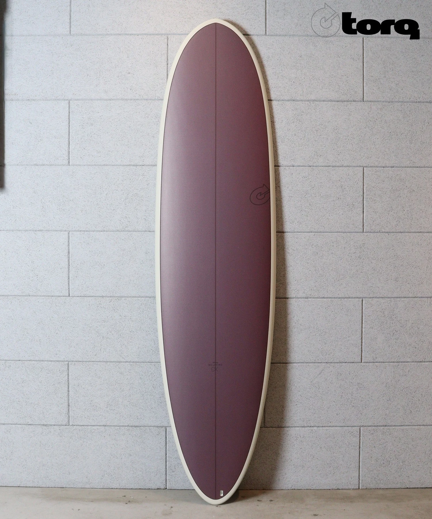 image - SHOP NEWS | ムラサキスポーツオンラインストア 通販 Purple surfboard with a cream edge standing upright against a gray cinder block wall, Torq logo in the corner.